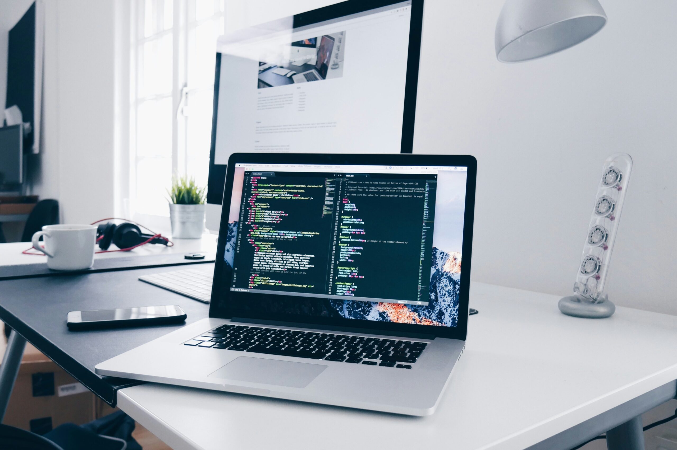 A MacBook with lines of code on its screen on a busy desk. Why your shouldn't choose cheap website hosting for wordpress.